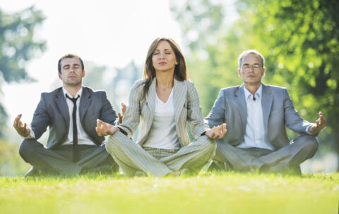Business people exercising yoga in park.