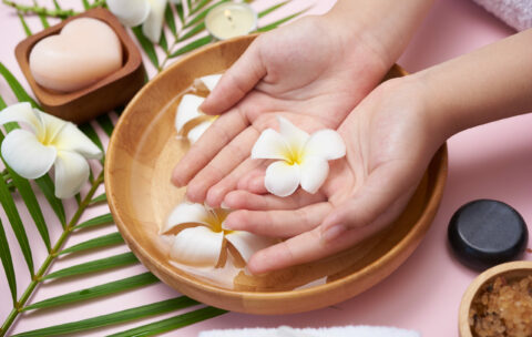 Woman soaking her hands in bowl of water and flowers, Spa treatm